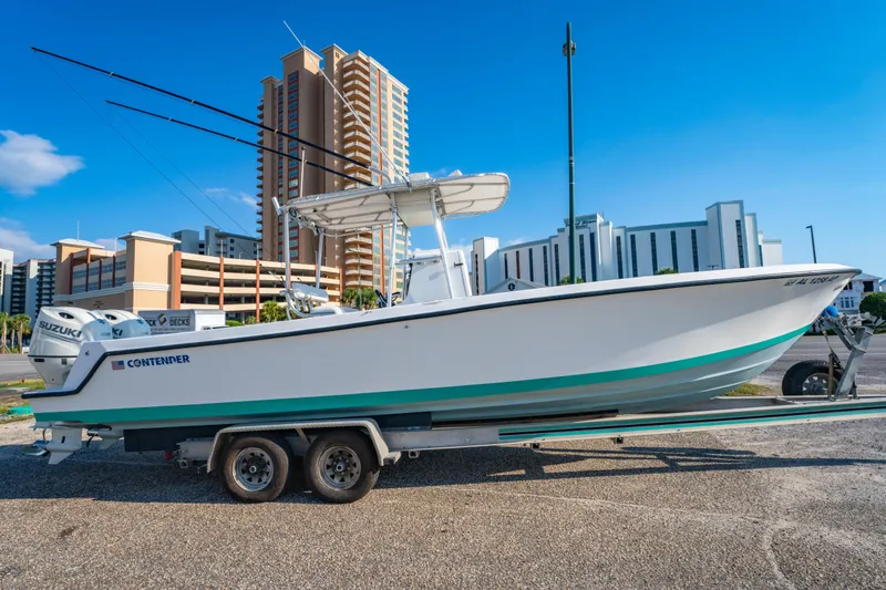 Slide: The Image of 1997 Contender 27 boat on trailer, cityscape background, clear blue sky. - 2