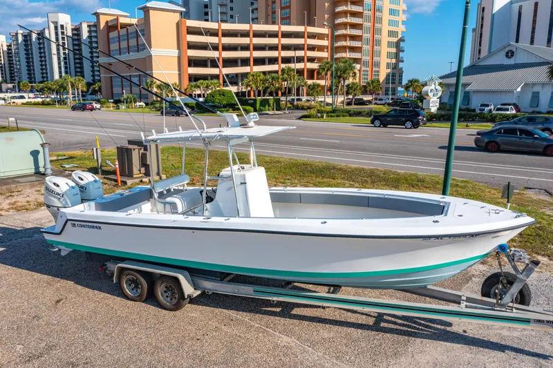 Slide: The Image of 1997 Contender 27 boat on trailer, parked near a road with buildings in the background. - 29