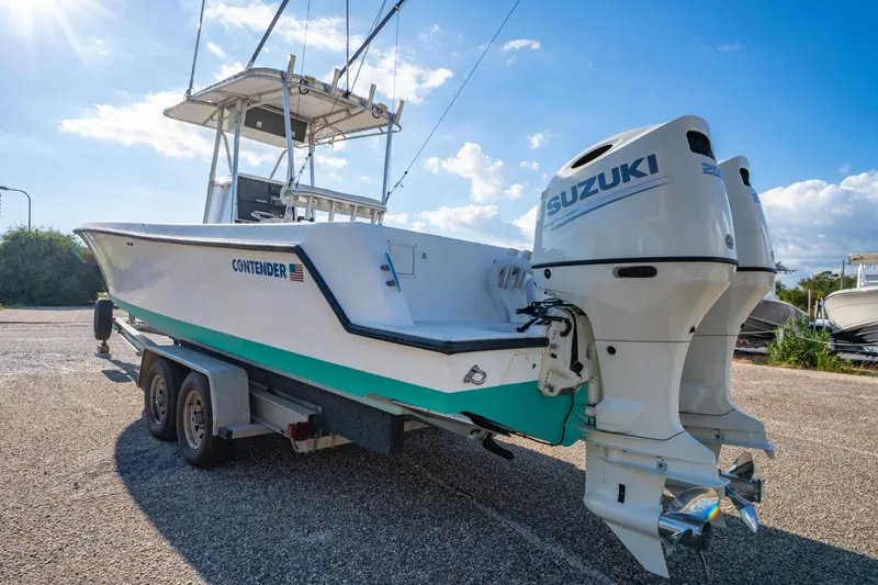 Slide: The Image of 1997 Contender 27 boat on trailer with dual Suzuki outboard engines, parked under blue sky. - 5