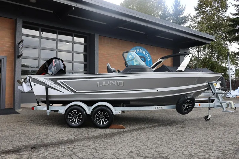 Slide: The Image of 2026 Lund 1875 Impact XS Sport boat on trailer, parked outside a garage. - 2