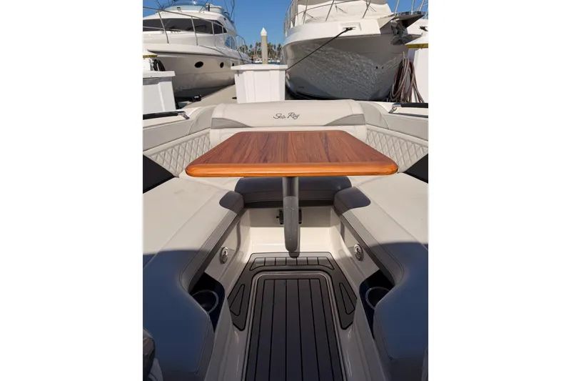 Slide: The Image of 2024 Sea Ray SLX 260 boat interior with wooden table and cushioned seating. - 58