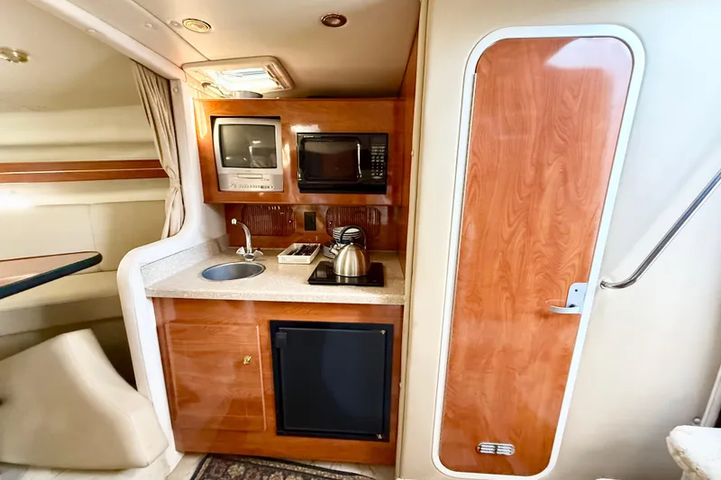 Slide: The Image of 2005 Rinker Fiesta Vee 300 interior with kitchenette, featuring sink, microwave, and wooden cabinetry. - 15