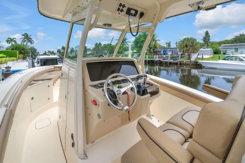 Slide: The Image of 2015 Scout 275 LXF boat interior with steering wheel, docked by a scenic canal. - 3