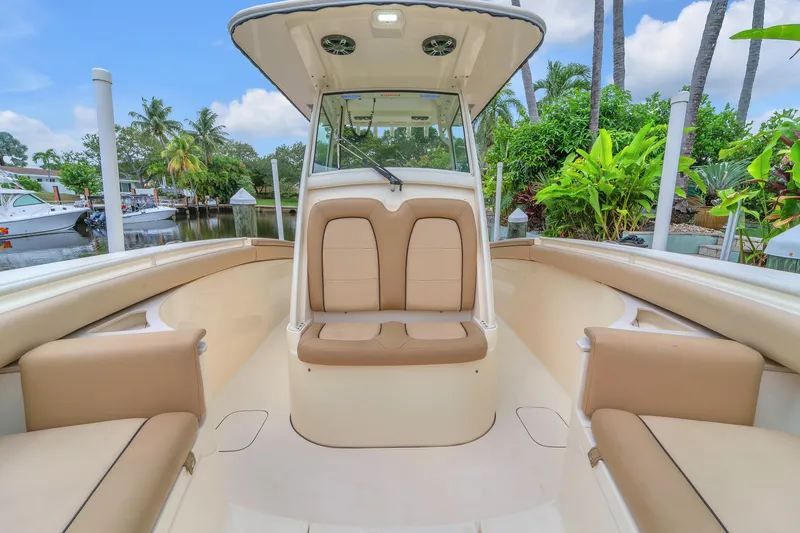 Slide: The Image of 2015 Scout 275 LXF boat interior with tan seating, docked near lush greenery. - 33