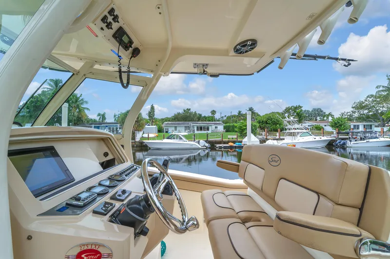 Slide: The Image of 2015 Scout 275 LXF boat interior with steering wheel and control panel, docked by waterfront homes. - 4