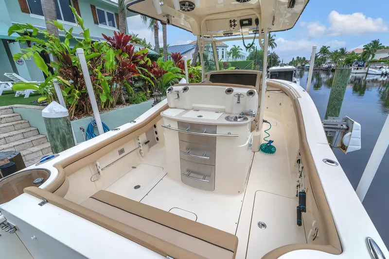 Slide: The Image of 2015 Scout 275 LXF boat interior with seating and console, docked by tropical plants. - 43