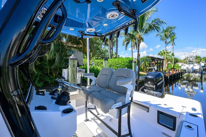 Slide: The Image of 2023 Sportsman Masters 247OE Bay Boat interior with seating and steering, docked near palm trees. - 20