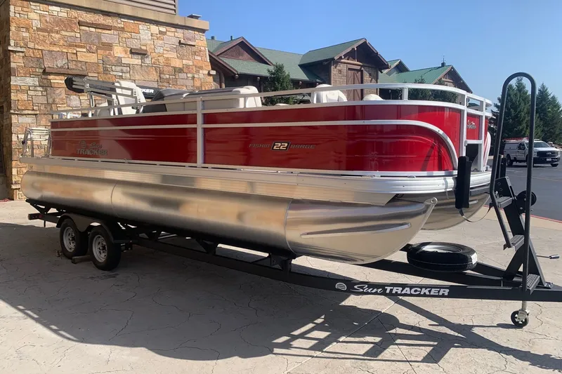 Slide: The Image of 2026 Sun Tracker Fishin' Barge 22 DLX pontoon boat on trailer, red and silver design. - 3