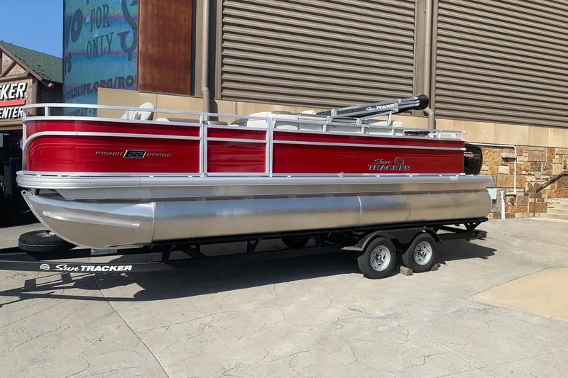 The Image of 2026 Sun Tracker Fishin' Barge 22 DLX pontoon boat on trailer, red and silver design. - 0