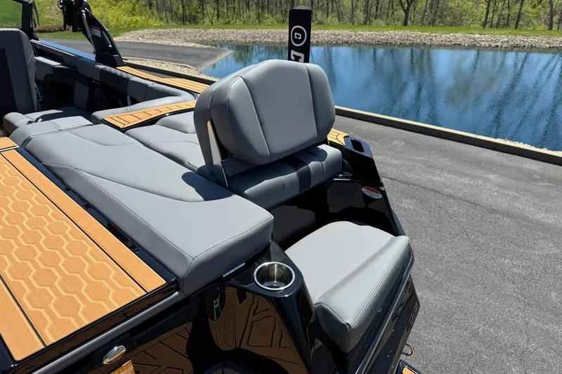 Slide: The Image of 2025 MasterCraft XT23 boat interior with gray seating and wood accents by a lake. - 13