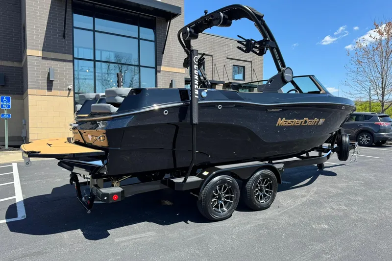 Slide: The Image of 2025 MasterCraft XT23 boat on trailer, parked outside a modern building. - 3