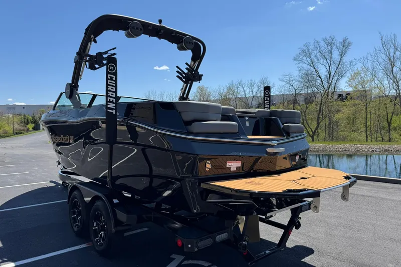Slide: The Image of 2025 MasterCraft XT23 boat with sleek black design, parked near a scenic lake. - 5