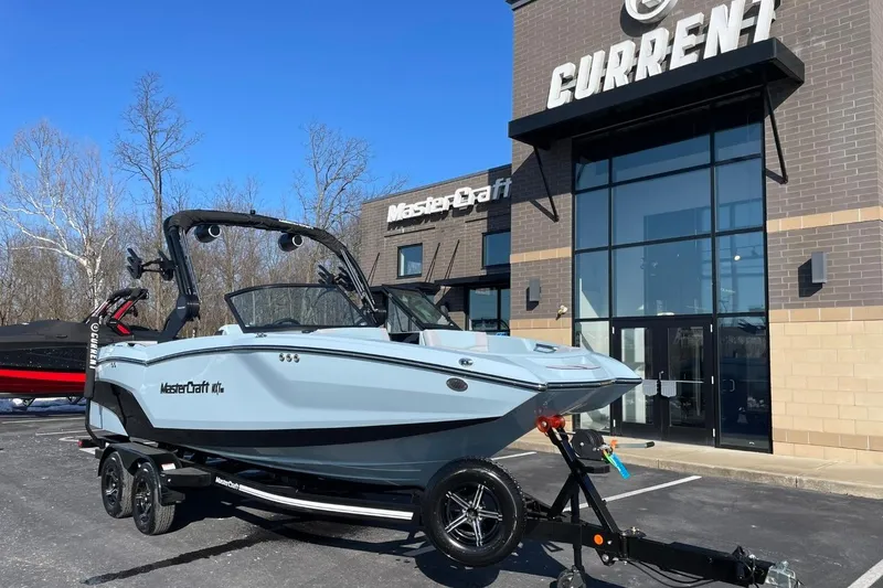 The Image of 2025 MasterCraft NXT22 boat on trailer outside dealership under clear blue sky. - 1