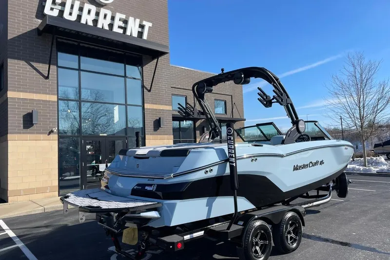 Slide: The Image of 2025 MasterCraft NXT22 boat on trailer outside dealership, sunny day. - 3