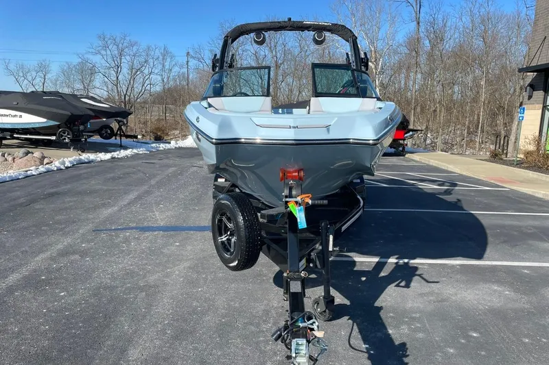 Slide: The Image of 2025 MasterCraft NXT22 boat on trailer in parking lot, clear blue sky background. - 8