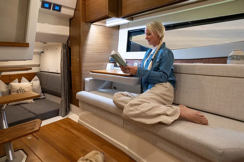Slide: The Image of Manufacturer Provided Image: Woman reading inside 2026 Boston Whaler 365 Conquest boat cabin, featuring modern interior design. - 28