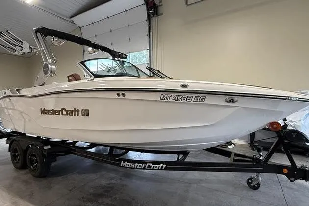 The Image of 2023 MasterCraft XT23 boat in garage, white exterior, on trailer. - 1