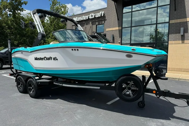 The Image of 2025 MasterCraft NXT20 boat in turquoise and white on a trailer outside dealership. - 1