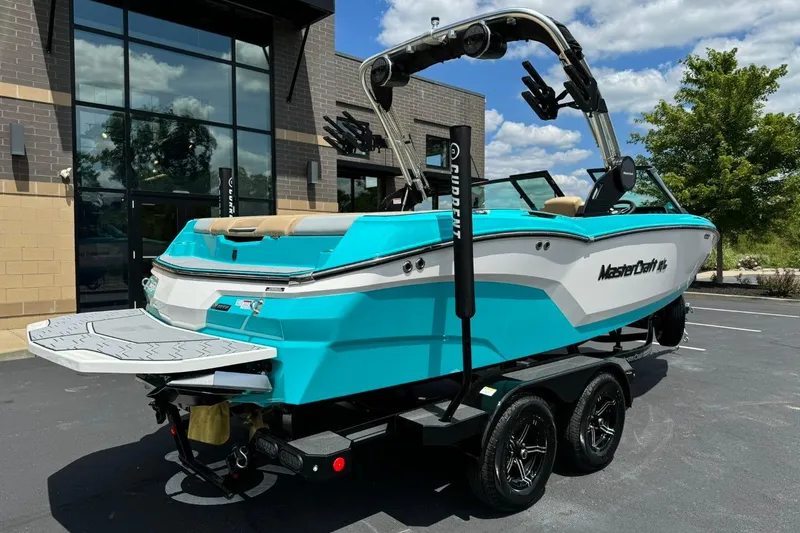 Slide: The Image of 2025 MasterCraft NXT20 boat in vibrant turquoise, parked outdoors on a trailer. - 3