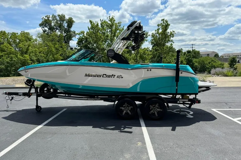 Slide: The Image of 2025 MasterCraft NXT20 boat on trailer, parked outdoors under a partly cloudy sky. - 6