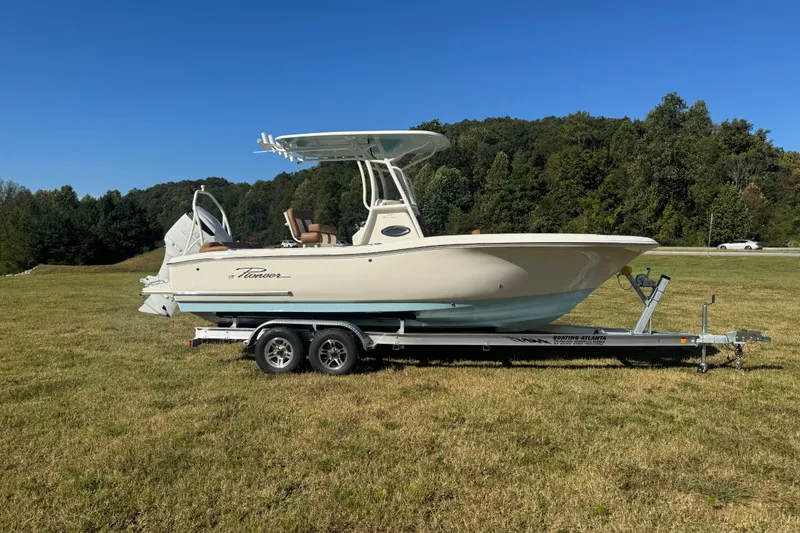 The Image of 2026 Pioneer 222 Islander boat on trailer, parked on grassy field with trees in background. - 0