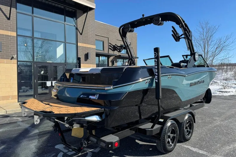 Slide: The Image of 2025 MasterCraft NXT23 boat on trailer, parked outside modern building. - 2