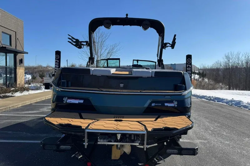 Slide: The Image of 2025 MasterCraft NXT23 boat, rear view, parked on snowy pavement under clear blue sky. - 4