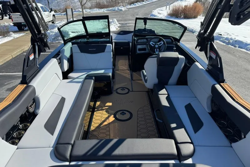 Slide: The Image of 2025 MasterCraft NXT23 boat interior with modern seating and steering, parked in snowy setting. - 7