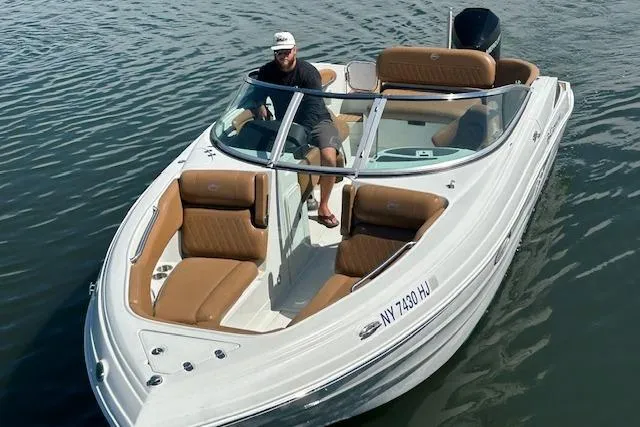 Slide: The Image of 2023 Crownline 250 XSS boat with tan seating on water, featuring a person at the helm. - 2