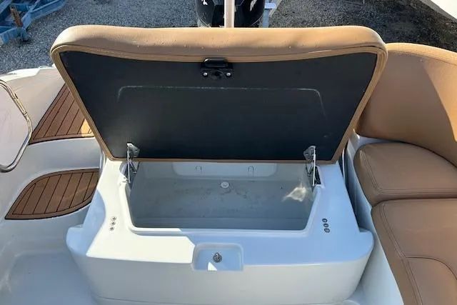 Slide: The Image of 2023 Crownline 250 XSS boat storage compartment with open lid and tan seating. - 9