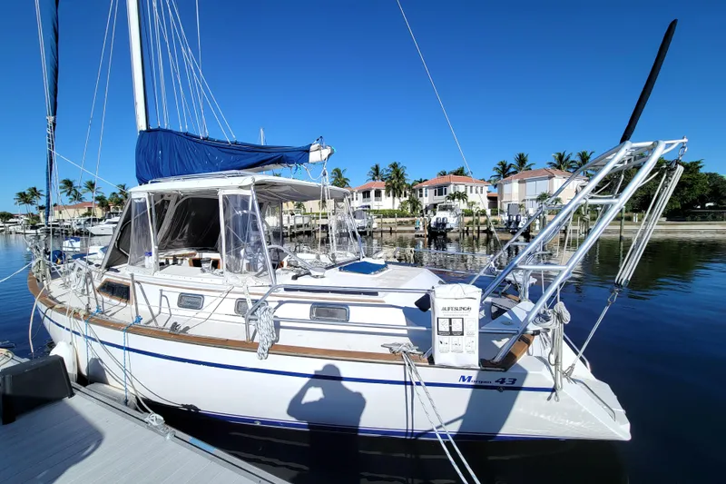 Slide: The Image of 1987 Morgan 43 CC sailboat docked in a sunny marina, surrounded by palm trees. - 6