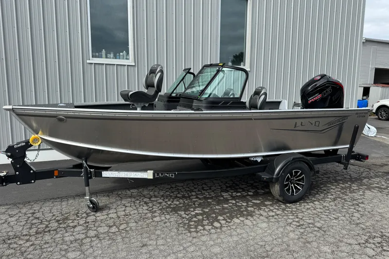 The Image of 2026 Lund 1800 Explorer Sport boat on trailer, parked outside a metal building. - 1