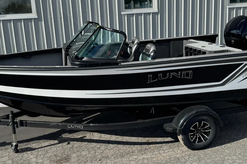 The Image of 2026 Lund 1875 Fisherman boat, black and white, parked on a trailer outside a building. - 1
