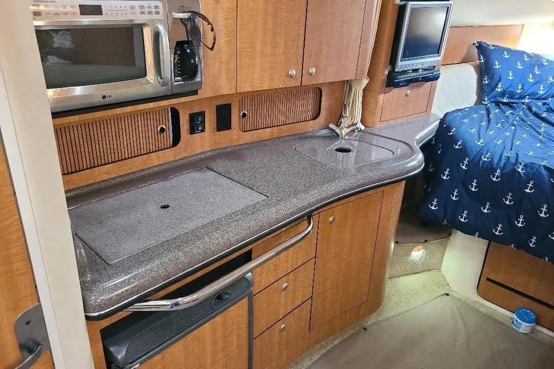 Slide: The Image of 2006 Sea Ray 320 Sundancer interior with kitchenette, microwave, and cozy bed with anchor-themed bedding. - 7