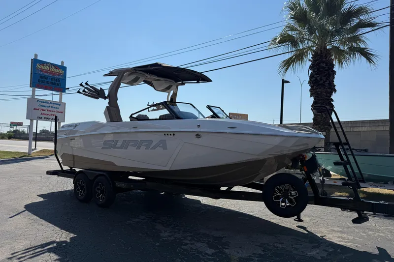 Slide: The Image of 2026 Supra SL 450 boat on trailer, parked near palm tree and signage. - 1