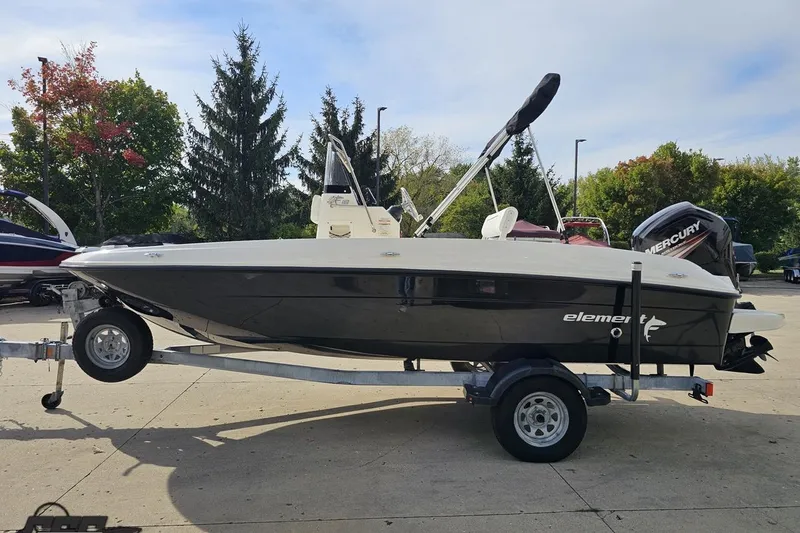 Slide: The Image of 2016 Bayliner Element F18 boat on trailer, parked outdoors with trees in background. - 28