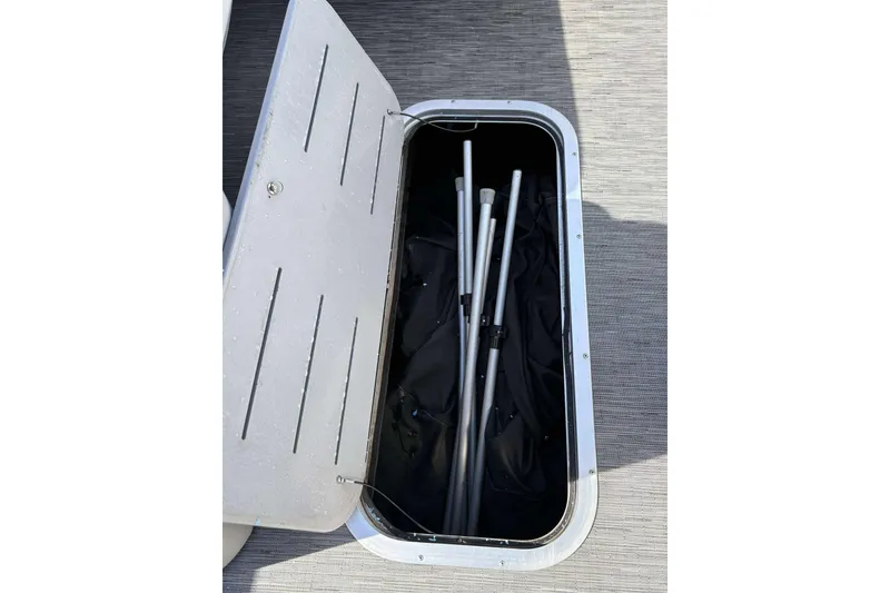 Slide: The Image of Open storage compartment on 2021 Bennington 27RX boat, containing metal poles. - 17