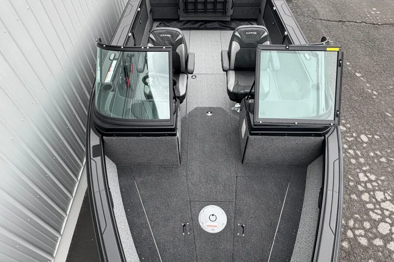 Slide: The Image of 2026 Lund 2075 Fisherman boat interior with dual seats and windshield, docked beside a building. - 3
