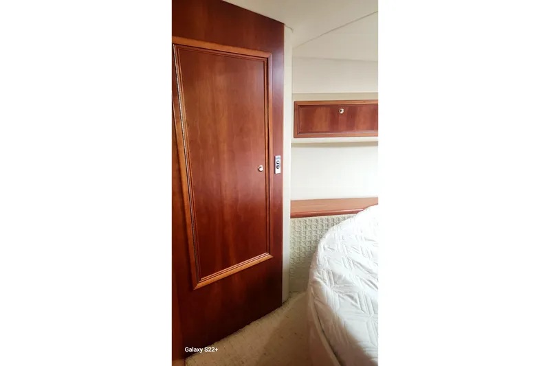 Slide: The Image of Interior of 2006 Riviera 47 Open Flybridge Series II, featuring wooden door and cozy bedding. - 54