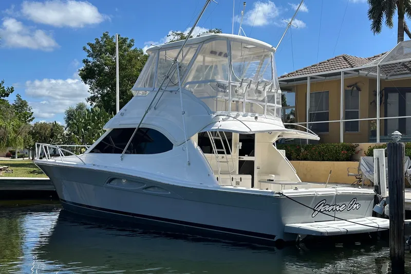 The Image of 2002 Riviera 40 Flybridge yacht docked by a waterfront home under a clear blue sky. - 0
