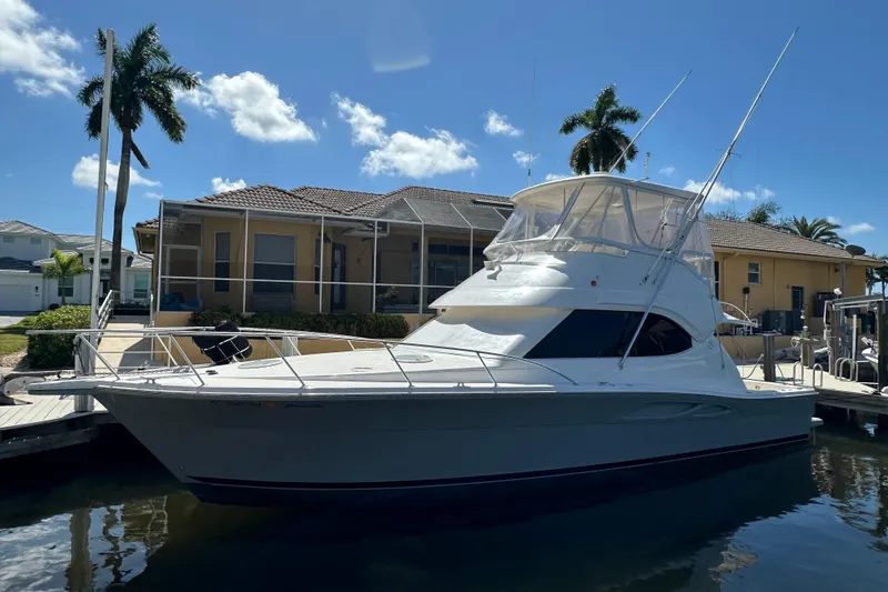 Slide: The Image of 2002 Riviera 40 Flybridge yacht docked by a waterfront home under a clear blue sky. - 3