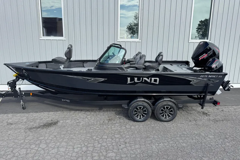 Slide: The Image of 2026 Lund 2075 Impact XS boat, black exterior, parked on a trailer beside a building. - 1