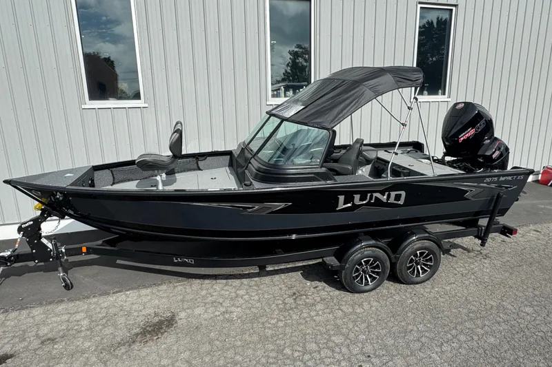 Slide: The Image of 2026 Lund 2075 Impact XS boat, black exterior, parked on a trailer outside a building. - 2