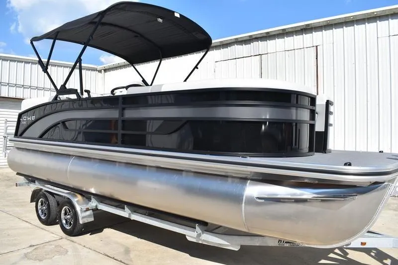 Slide: The Image of 2026 Lowe SS 230 pontoon boat on trailer, black canopy, parked by warehouse. - 3