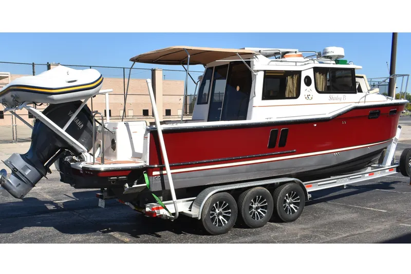 Slide: The Image of 2024 Ranger Tugs R-27 boat on trailer, red and white exterior, parked outdoors. - 2