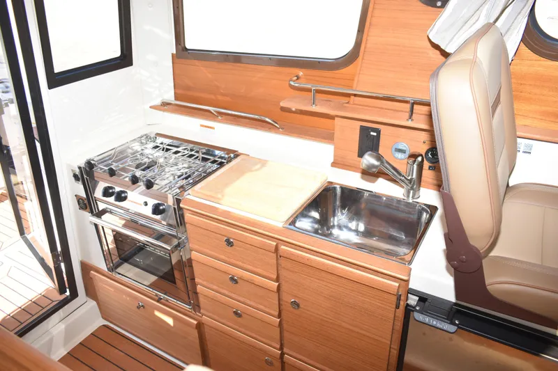 Slide: The Image of 2024 Ranger Tugs R-27 interior kitchen with stove, sink, and wooden cabinetry. - 28