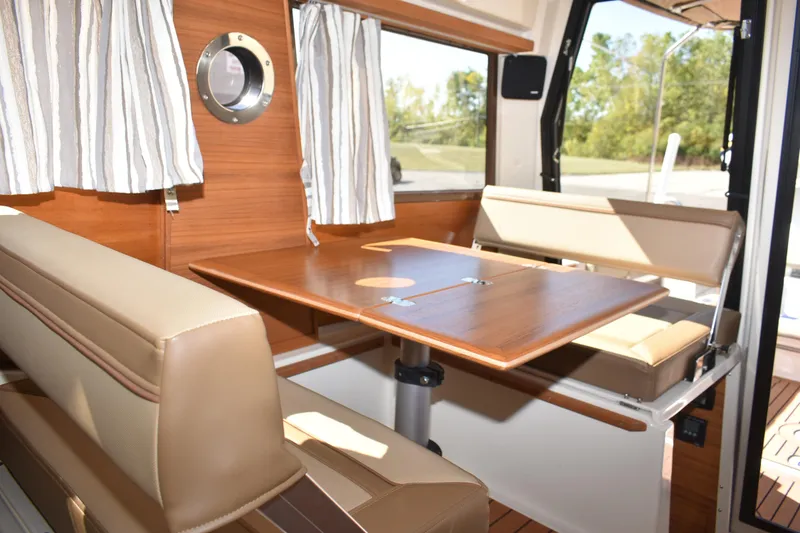 Slide: The Image of 2024 Ranger Tugs R-27 interior with wood table, beige seating, and striped curtains. - 29
