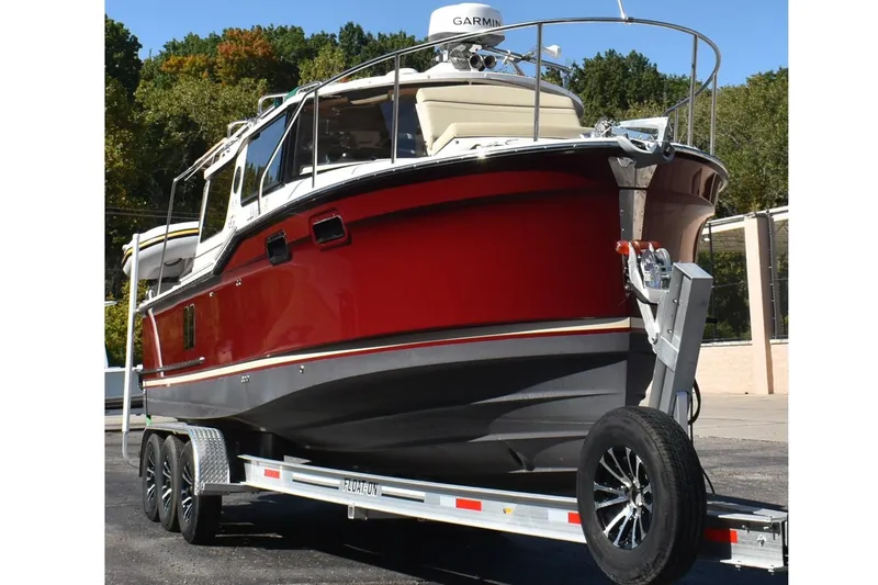 Slide: The Image of 2024 Ranger Tugs R-27 boat on trailer, red hull, parked outdoors. - 3