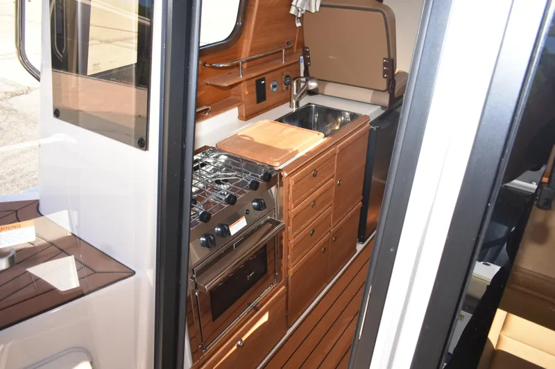 Slide: The Image of 2024 Ranger Tugs R-27 interior kitchen with stove, sink, and wooden cabinetry. - 31