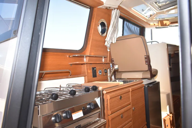 Slide: The Image of 2024 Ranger Tugs R-27 interior kitchen with stove, sink, and wooden cabinetry. - 33